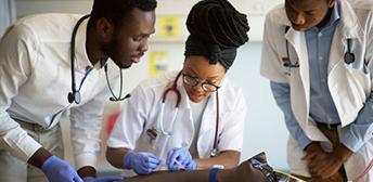 A group of people in white lab coats training to draw blood on a test medical device