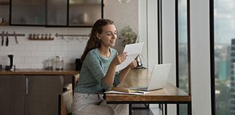 A woman sitting at a counter reading a piece of paper in front of her computer
