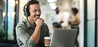 A male employer wearing headphones and sitting at a table with a computer paying his taxes