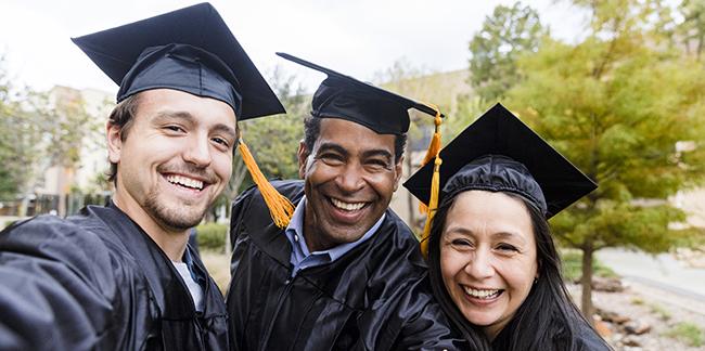 A group of adults smiling in a photo at their graduation ceremony. They are wearing caps and gowns. 