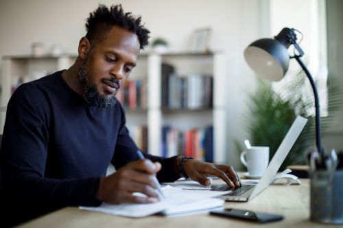 Man writing on paper and using laptop computer