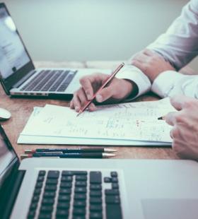 Two people working at a desk with their laptops open