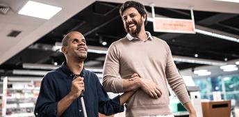 A seeing man leading a blind man using a cane.